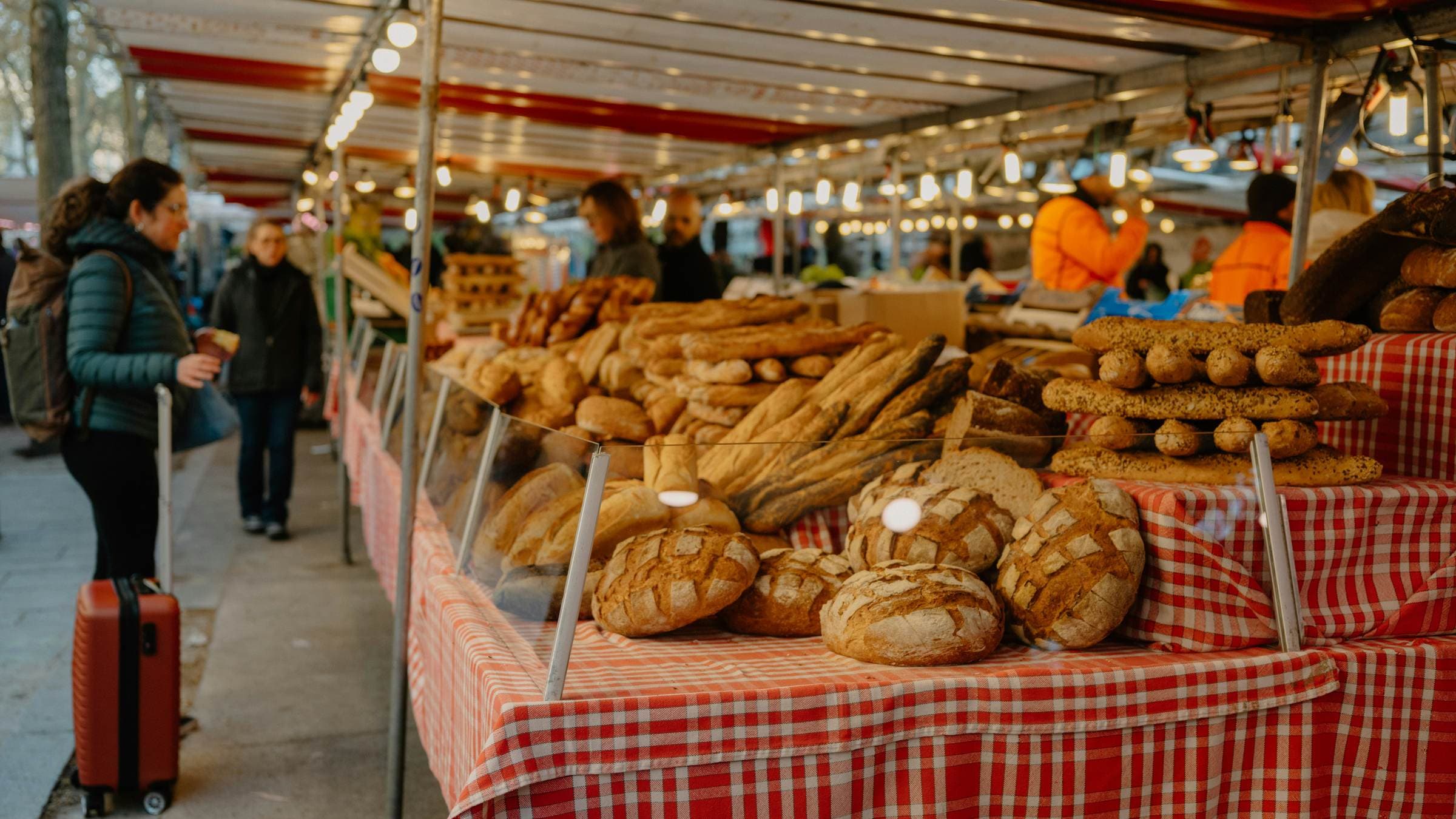 A bread stall under an awning, mid-morning, a customer deciding
