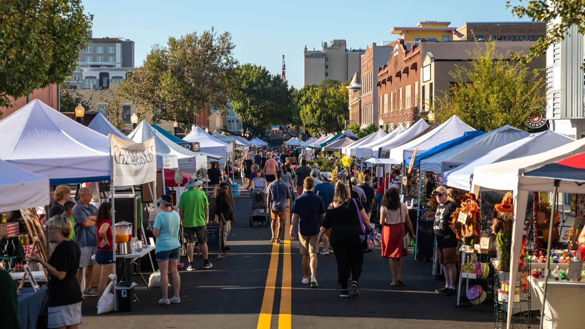 A market morning: canopies down both sides of a closed street, and a crowd walking between them