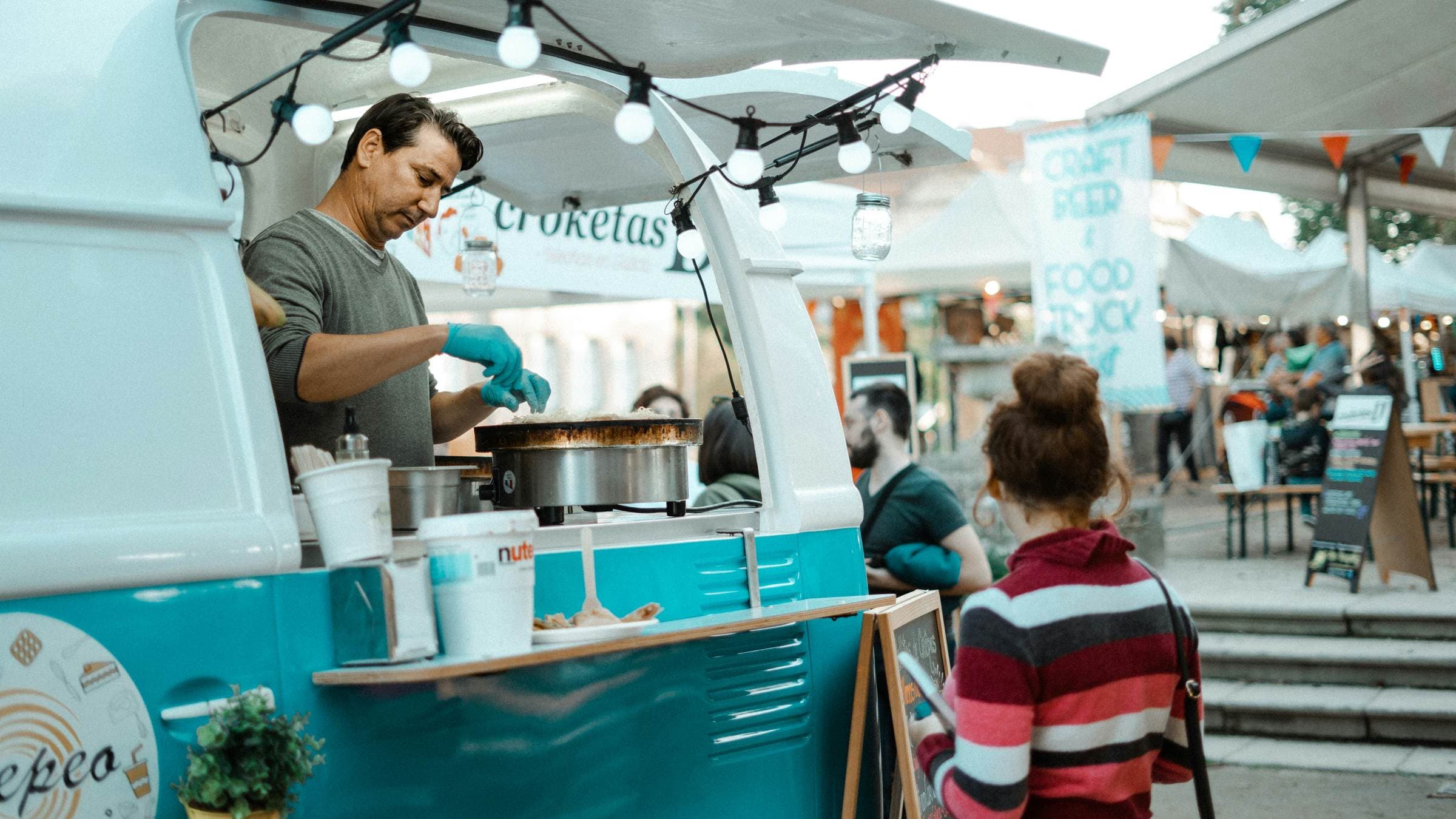 A food vendor serving from a truck at a market, a customer waiting